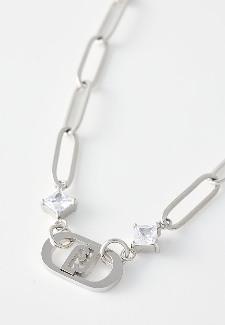 Collier en chaîne argentée avec des maillons allongés, deux pierres précieuses carrées transparentes et un pendentif central au logo. Texture lisse, design géométrique moderne.