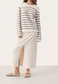 Pull rayé crème et taupe, associé à une jupe longue beige clair avec une fente devant. Porté avec des sandales plates.