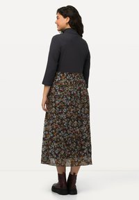 Sukienka maxi z jednolitą ciemną górą i spódnicą w kwiatowy wzór. Spódnica jest przezroczysta, z warstwami falbanek, zestawiona z botkami za kostkę.