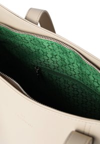 Beige nahkahandbag, jossa on vihreä kuvioitu vuori, varustettuna vetoketjulla ja sisällä vetoketjullisella taskulla.
