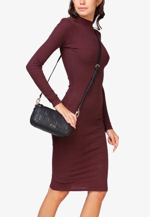 Borsa a tracolla nera trapuntata con hardware dorato, tracolla regolabile e forma arrotondata. Il modello indossa un vestito a maniche lunghe a coste di colore borgogna.