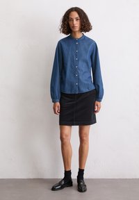 Jeanshemd mit rundem Kragen, langen Ärmeln und schwarzem Baumwollrock. Schwarze Slipper und Socken runden das Outfit ab.