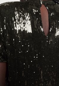 Svart paljettyg med en strukturerad yta, som har korta ärmar och en nyckelhålsöppning på baksidan som reflekterar ljus.