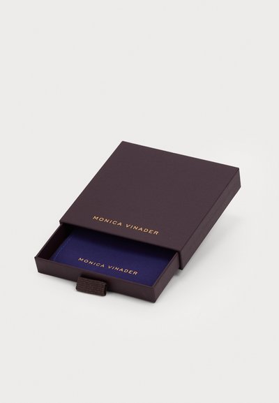 Scatola di cartone viola con lettere dorate, parzialmente aperta, che rivela un rivestimento interno blu. La scatola presenta una linguetta in tessuto per una facile apertura.