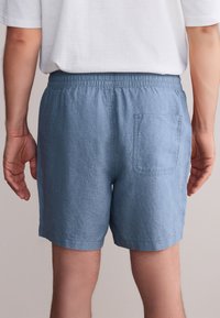 Pantaloncini di lino azzurro chiaro con vita elasticizzata, caratterizzati da una singola tasca a toppa posteriore e una vestibilità comoda. Il tessuto lavorato sembra traspirante.