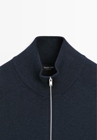 Dunkelblauer, gestrickter Reißverschluss-Pullover mit hohem Kragen, mit gerippter Struktur und einem silbernen Reißverschluss, Markenetikett sichtbar am Krageninneren.