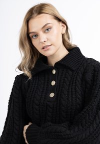 Pullover nero in maglia con un motivo a treccia spesso, colletto ampio e tre bottoni dorati decorativi sulla parte anteriore.