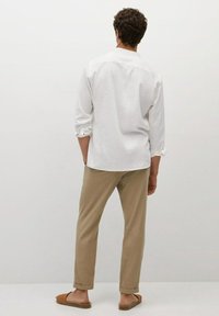 Witte blouse met lange mouwen en opgerolde manchetten, gecombineerd met beige broek. Opvallend detail: bruine instap sandalen.