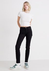 Svarta skinny jeans i denim med fem fickor och midjehöjd, matchade med en figurnära vit kort t-shirt och ljusa sneakers.