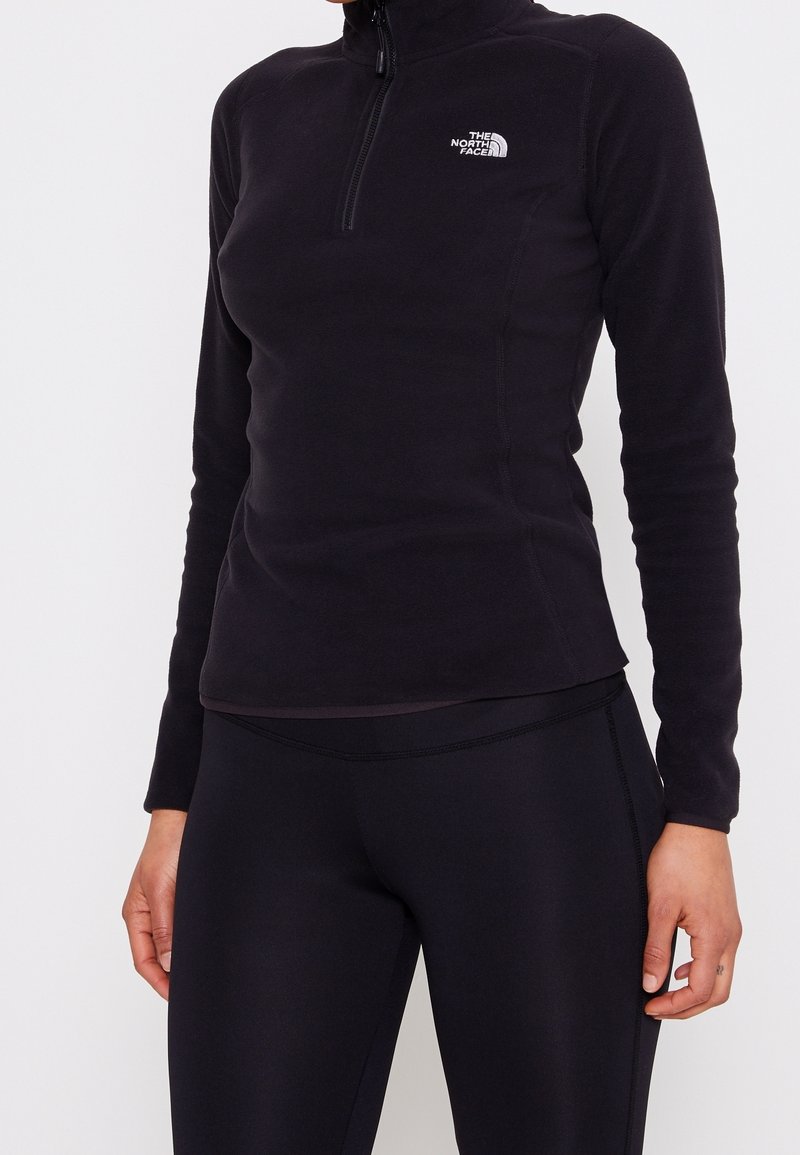 Pullover in pile nero con colletto alto e zip quarti, caratterizzato da un piccolo logo bianco sul lato sinistro del petto e maniche lunghe.