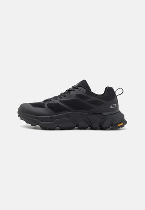 Schwarzer Sportschuh mit Mesh-Einsätzen, dicker, gepolsterter Sohle, Schnürung vorne, Zuglasche an der Ferse und Vibram-Logo an der Außensohle.