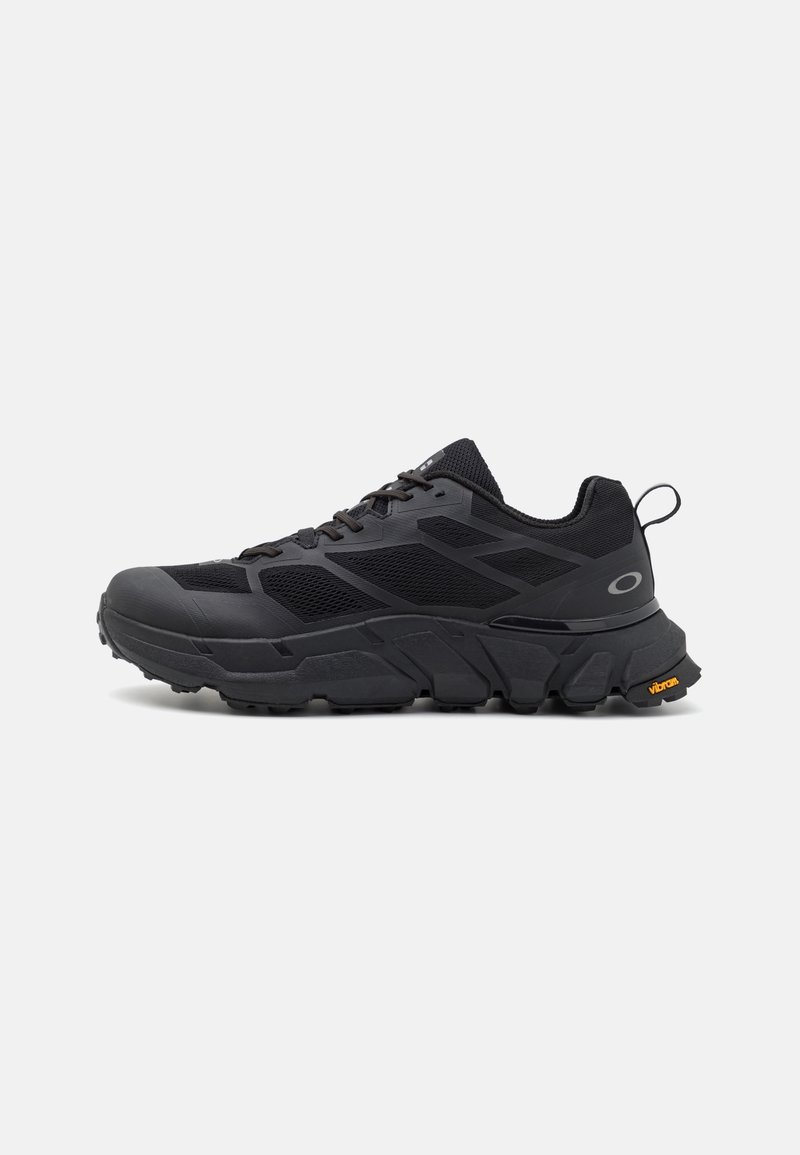 Baskets de sport noires avec des panneaux en mesh, semelle épaisse et rembourrée, fermeture à lacets à l'avant, languette au talon et logo Vibram sur la semelle extérieure.