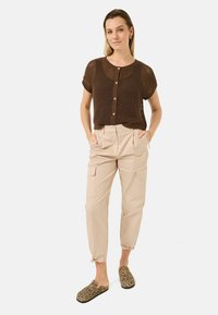 Top corto lavorato a maglia marrone con bottoni, pantaloni cargo beige a vita alta con tasche e scarpe slip-on con stampa leopardata.