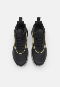 Zapatillas deportivas negras con parte superior de malla, acentos amarillos y suela de goma texturizada, con un diseño de cordones y una pestaña en el talón.