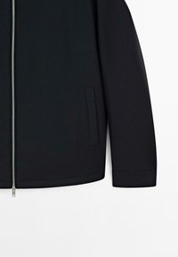Black jacket with a smooth, matte finish, featuring a front zipper, a stand collar, and side pockets. Plain design with clean lines.