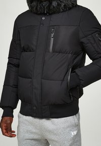 Czarna pikowana kurtka puchowa z kołnierzem z sztucznego futra, wyposażona w kieszenie na suwak, zapięcie na guziki oraz pikowany wzór. Miękka tkanina o gładkiej fakturze.