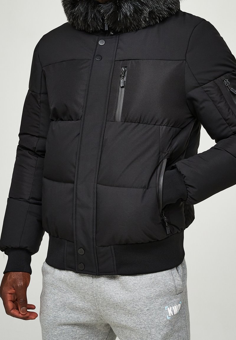 Czarna pikowana kurtka puchowa z kołnierzem z sztucznego futra, wyposażona w kieszenie na suwak, zapięcie na guziki oraz pikowany wzór. Miękka tkanina o gładkiej fakturze.