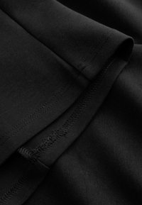 Gros plan d’un tissu noir montrant des coutures superposées et des détails de piqûres sur un tissu plié.