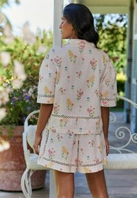 Floral-patterned, light-colored fabric set featuring a short-sleeve top and shorts with lace accents. Soft texture and relaxed fit.