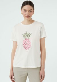 White cotton t-shirt featuring a pink and green pineapple graphic. Short sleeves and a round neckline. Smooth texture, casual fit.