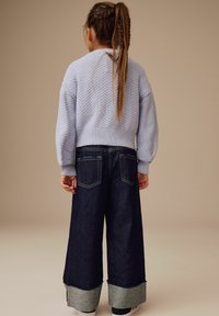 Hellblau strukturierter Strickpullover mit geripptem Saum, kombiniert mit weit geschnittenen dunkelblauen Jeanshosen mit umgeschlagenen Säumen und Gesäßtaschen.
