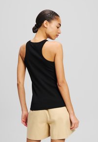 Schwarzes ärmelloses Tanktop mit geripptem Textur, rundem Ausschnitt und Racerback-Design, kombiniert mit beigen Shorts.