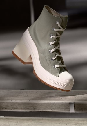 Sneaker montante en tissu vert clair avec capuchon blanc, talon épais blanc et semelle en caoutchouc texturée. Design à lacets avec œillets en argent.