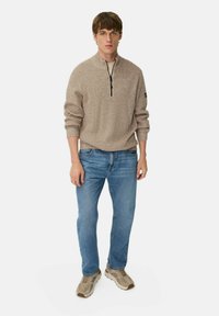 Beige gebreide pullover met een half-rits kraag, gecombineerd met lichtblauwe spijkerbroeken. Gemaakt met beige sneakers, voorzien van textuurdetails.