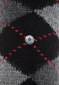 Calzino lavorato a maglia con motivo in nero, grigio e rosso, caratterizzato da forme a rombo e un bottone in metallo con logo. Tessuto morbido con filati a contrasto.