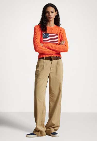 Narancssárga, kötött pulóver amerikai zászló mintával, világosbarna, széles szárú nadrággal és sötétkék, könnyen felvehető cipővel párosítva.