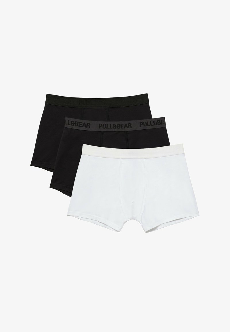 Trois paires de boxers pour hommes, deux noirs avec ceintures de marque et un blanc, disposés en couches sur un fond blanc.