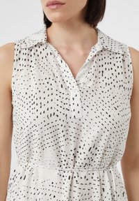 Ärmelloses Kleid aus leichtem Stoff mit einem Kragen und einem Muster aus schwarzen Punkten und Linien auf weißem Hintergrund.