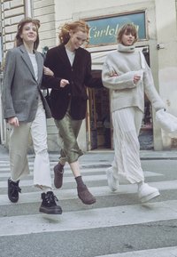 Tři mladé ženy, které se drží armády v armádě, se usmívají a kráčejí přes městský přechod v ležérních stylových oblečeních.