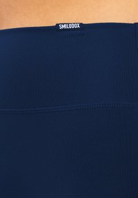 Top sportivo blu navy con una texture liscia, dotato di un'etichetta rettangolare con il nome del marchio "SMILODOX" sul retro.