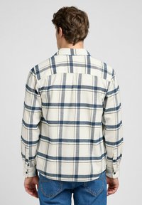 Camisa de franela de botones en cuadros crema y azul marino, con mangas largas, un dobladillo recto y una tela suave y texturizada.