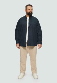 Dunkelblauses Button-Up-Hemd mit lässiger Passform, Brusttaschen und einer weichen Textur, kombiniert mit beigen Hosen und weißen Sneakers.