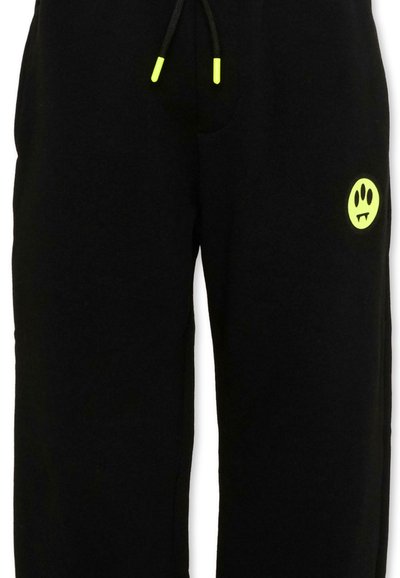 Pantalon de survêtement noir avec embouts de cordon de serrage jaune néon et petit logo smiley jaune néon avec des crocs sur la partie supérieure de la cuisse droite.