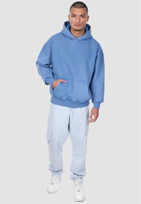 Blå bomulds hoodie med en frontlomme, ribbede ærmer og kant. Knapper til lyseblå denimjeans og hvide sneakers. Enkel, afslappet stil.