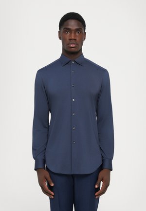 Chemise à manches longues bleu marine en tissu lisse, avec un col pointu, une fermeture à boutons à l'avant et un ourlet arrondi.