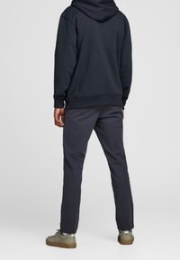 Sudadera con capucha en color azul marino, con puños y dobladillo acanalados; combinada con pantalones rectos oscuros. El calzado es marrón claro con un mínimo de detalles.
