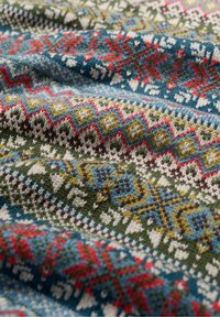 Strickstoff mit bunten nordischen Mustern in Rot, Blau, Grün, Weiß und Braun, der Schneeflocken und geometrische Formen zeigt.