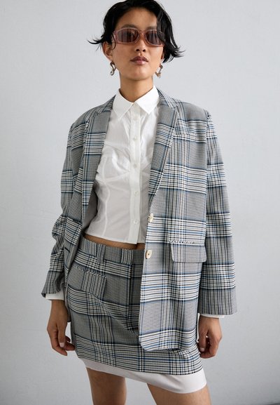Checkered blazer in shades of blue and grey, paired with a white button-up shirt and a matching mini skirt. Accessories include oversized sunglasses.