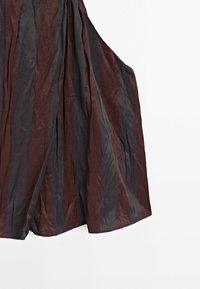 Vêtement en tissu rayé verticalement marron foncé et noir avec des jambes larges, présenté sur un fond blanc.