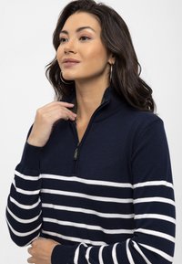 Pull à zip bleu marine avec des rayures horizontales blanches, des poignets côtelés et un col zippé. Matière texturée et coupe décontractée.