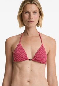 Bikini vrh z rdečim vzorcem, ki ima trikotno obliko, vezanje za vrat in bronast okrasni element na sredini.