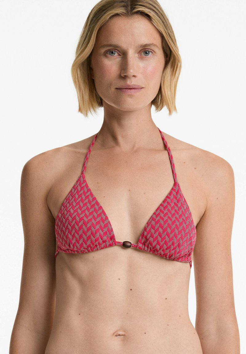 Bikini vrh z rdečim vzorcem, ki ima trikotno obliko, vezanje za vrat in bronast okrasni element na sredini.