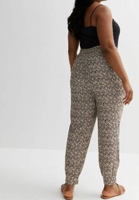Leichte, gemusterte Hosen in Beige mit schwarz-weißem Zickzackdesign; elastischer Bund und schmal zulaufende Bündchen; kombiniert mit einem schwarzen Oberteil und Sandalen.