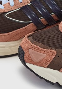 Gros plan de chaussures de sport en daim marron et rose avec un tissu côtelé, des semelles en caoutchouc noir et des lacets bleu clair.