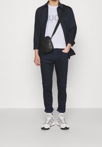 Mørkeblå skjorte med knapper over en hvid T-shirt, parret med slim-fit mørkeblå bukser og grå-hvide sneakers. Sort crossover taske med detaljer.