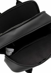 Melnā mugursoma ar atvērtu galveno nodalījumu, vienu iekšējā rāvējslēdzēja kabatu un redzamām baltām kopšanas etiķetēm iekšpusē.